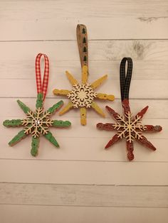 three wooden snowflakes hanging on a white wood plank wall with red, green and yellow ribbons