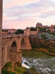 an old stone bridge over a river with buildings in the background and water running under it