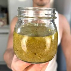 a man holding up a jar filled with something green and yellow in it's hand