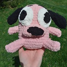 a hand holding a pink and black stuffed animal with eyes on it's face