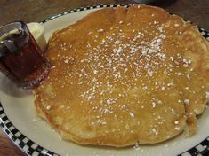 pancakes with syrup and butter on a plate next to a glass of beer or soda