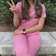 a woman in pink scrubs is sitting on a bench and making the peace sign