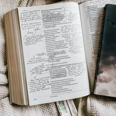 an open book sitting on top of a bed next to a pen and paper with writing