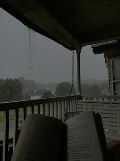 an open book sitting on top of a porch next to a window covered in rain