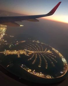 an airplane wing flying over the city lights at night in the sky above the ocean