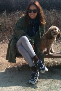 a woman is sitting on a bench with her dog in front of her and smiling