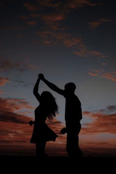 the silhouette of two people are dancing in front of an orange and black sky at sunset