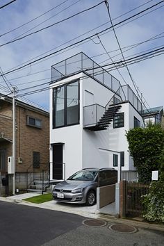 a car parked in front of a white building with stairs on the side and cars parked outside