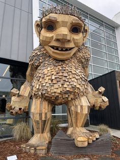 a wooden sculpture of a bear with spikes on it's head and arms, standing in front of a building