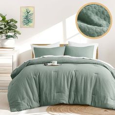 a bed with green comforter and pillows in a room next to a plant on the floor