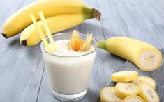 there is a glass with some fruit in it and two bananas on the table next to it