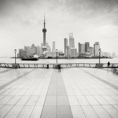 black and white photograph of people walking near the water in front of a cityscape