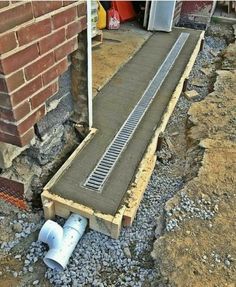 a drain in the ground next to a brick wall and some pipes on top of it