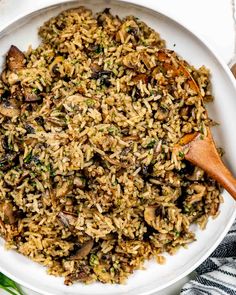 a white bowl filled with rice and mushrooms on top of a table next to a wooden spoon