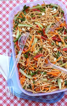 a plastic container filled with noodles and veggies on top of a checkered table cloth