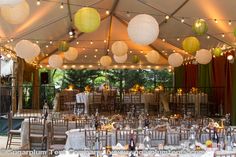 tables and chairs are set up under the tent for an outdoor wedding reception with paper lanterns hanging from the ceiling