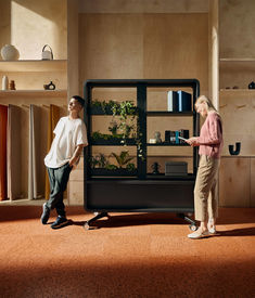 two people are standing in front of a shelf with plants on it and one person is looking at the shelves