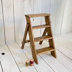 a wooden step stool next to spools of thread on a white wood floor