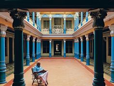 a man sitting on a chair in an empty building with columns and pillars around him