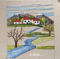 a cross stitch pattern with houses on the hill and river running through it in front of a mountain range