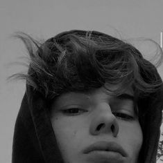 a young man wearing a hoodie with his hair blowing in the wind and looking off into the distance