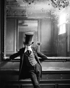 a man in a top hat and coat leaning against a wall