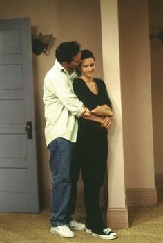 a man and woman standing next to each other in front of a door with their arms around each other