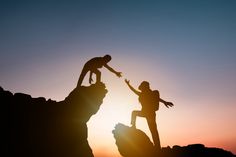 two people reaching out to each other on top of a mountain at sunset or sunrise