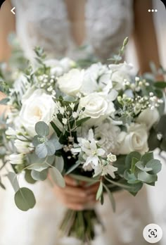 a bride holding a bouquet of white flowers and greenery