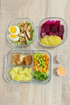 three plastic containers filled with food on top of a wooden table next to an egg, meat and veggies