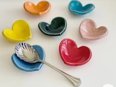 six heart shaped bowls with spoons in them on a white surface, one is empty