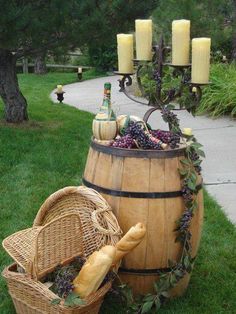 a wine barrel with candles and grapes in it sitting on the grass next to a basket