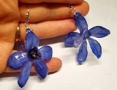 two blue flowers are being held up by someone's hand with earrings on them