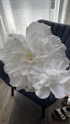 a large white flower sitting on top of a chair next to a pair of sandals