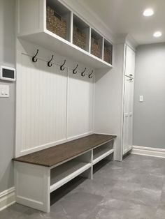 a white mud room with two benches and some baskets on the back wall, along with several coat racks