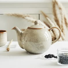 a white teapot sitting on top of a table next to two cups and spoons