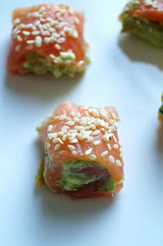 four sushi rolls with sesame seeds and salmon in them on a white table top