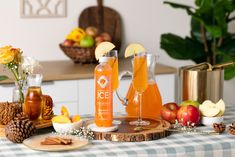 an assortment of fruits and drinks on a table with flowers, apples, cinnamons, pine cones, and other items