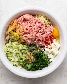 a white bowl filled with meat, vegetables and seasoning on top of a table