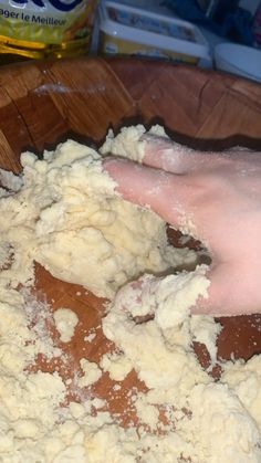 a person is kneading dough into a wooden bowl on the table with other ingredients