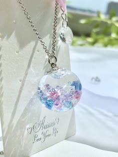 a clear glass ball with pink and blue flowers on it is hanging from a silver chain