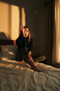 a woman sitting on top of a bed next to a window