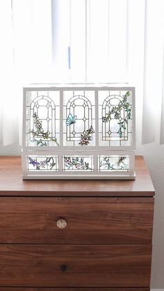 a stained glass window sitting on top of a wooden dresser next to a white curtain