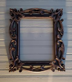 an ornate frame hanging on the side of a white painted wall with wood slats