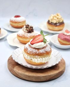 several pastries are arranged on small white plates with strawberries and other toppings