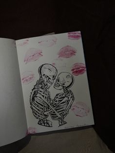 an open book with a drawing of two skeletons holding each other's hands and kissing