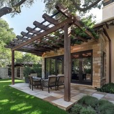 an outdoor dining area with table and chairs under a pergolated trellis on the lawn