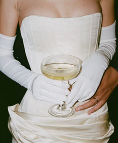 a woman wearing white gloves holding a wine glass in her right hand and the other arm wrapped around her waist