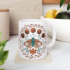 a coffee mug with a butterfly painted on the side and flowers around it sitting on a coaster