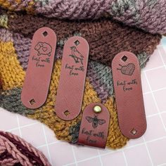 three leather bookmarks with words on them sitting next to a pile of knits